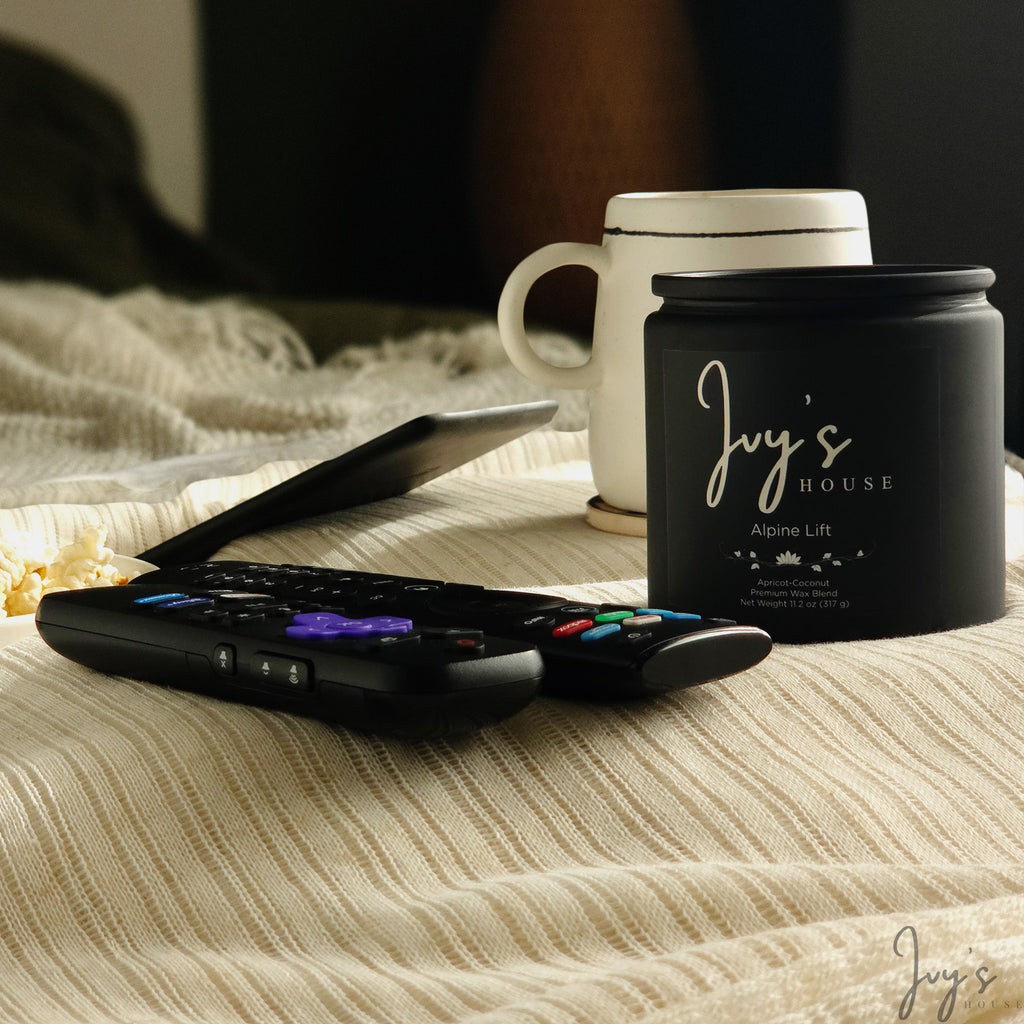 Ivy’s House Alpine Lift candle on a textured table beside a mug, tablet, and remotes in a cozy setting