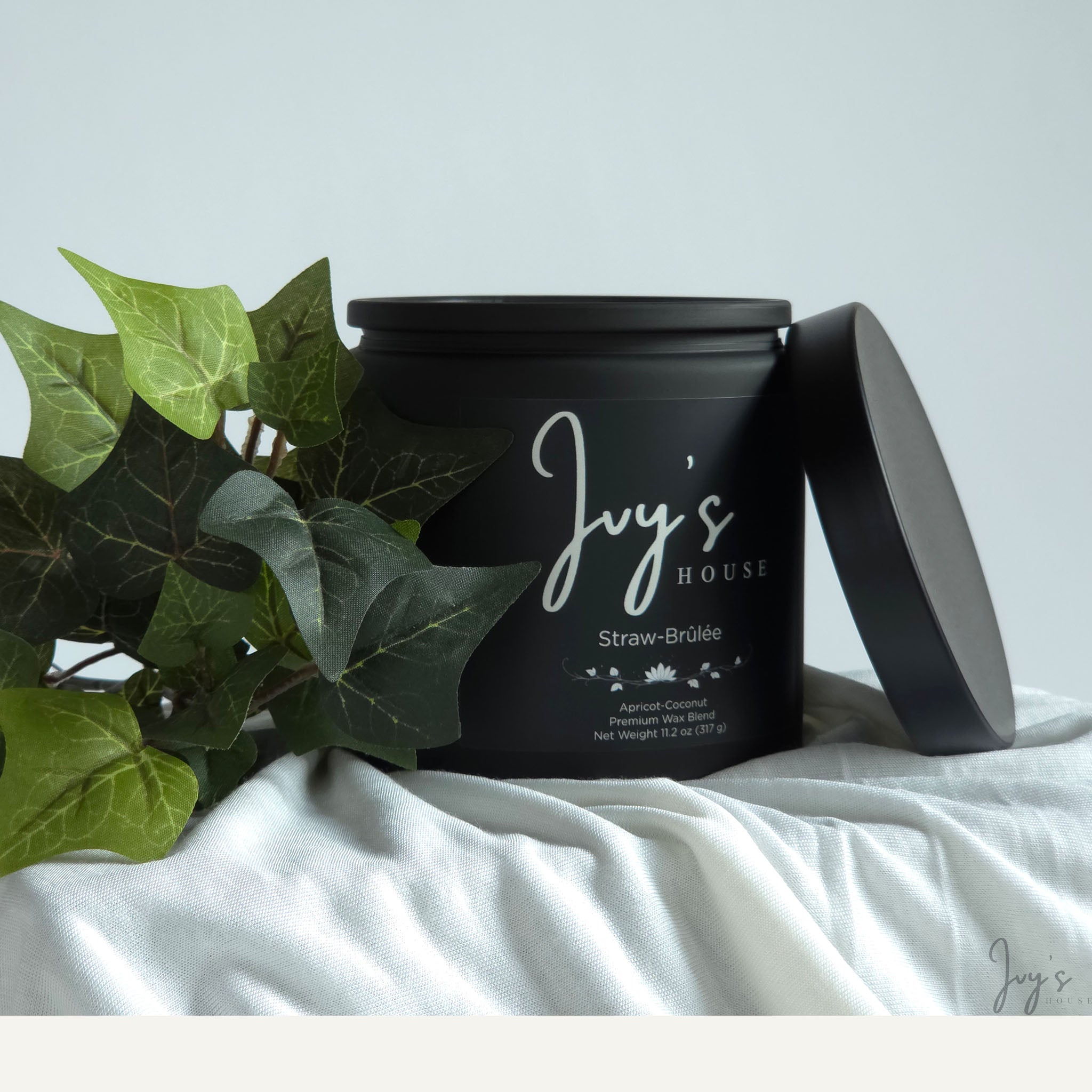 Straw-Brûlée premium scented candle by Ivy’s House with ivy leaves on soft white fabric