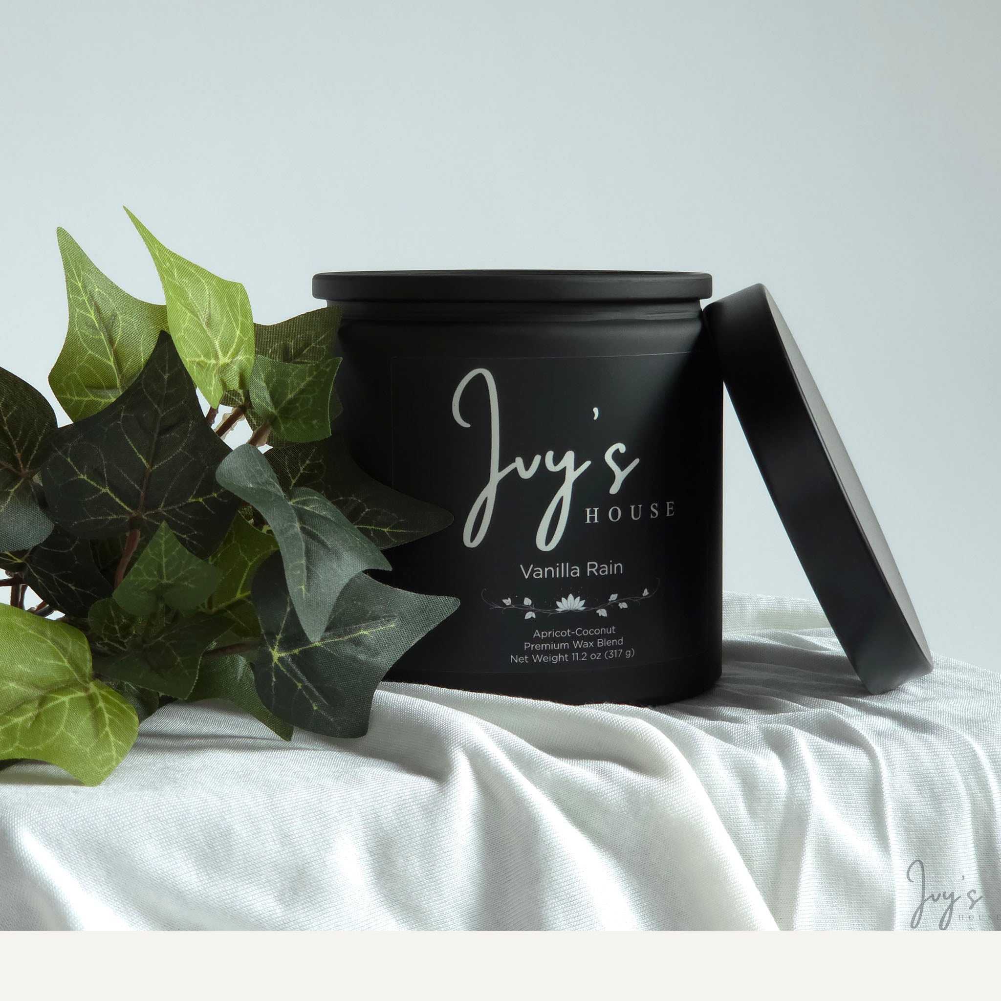 Vanilla Rain premium scented candle by Ivy’s House with ivy leaves on soft white fabric