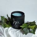 Vanilla Rain premium scented candle by Ivy’s House with ivy leaves on soft white fabric