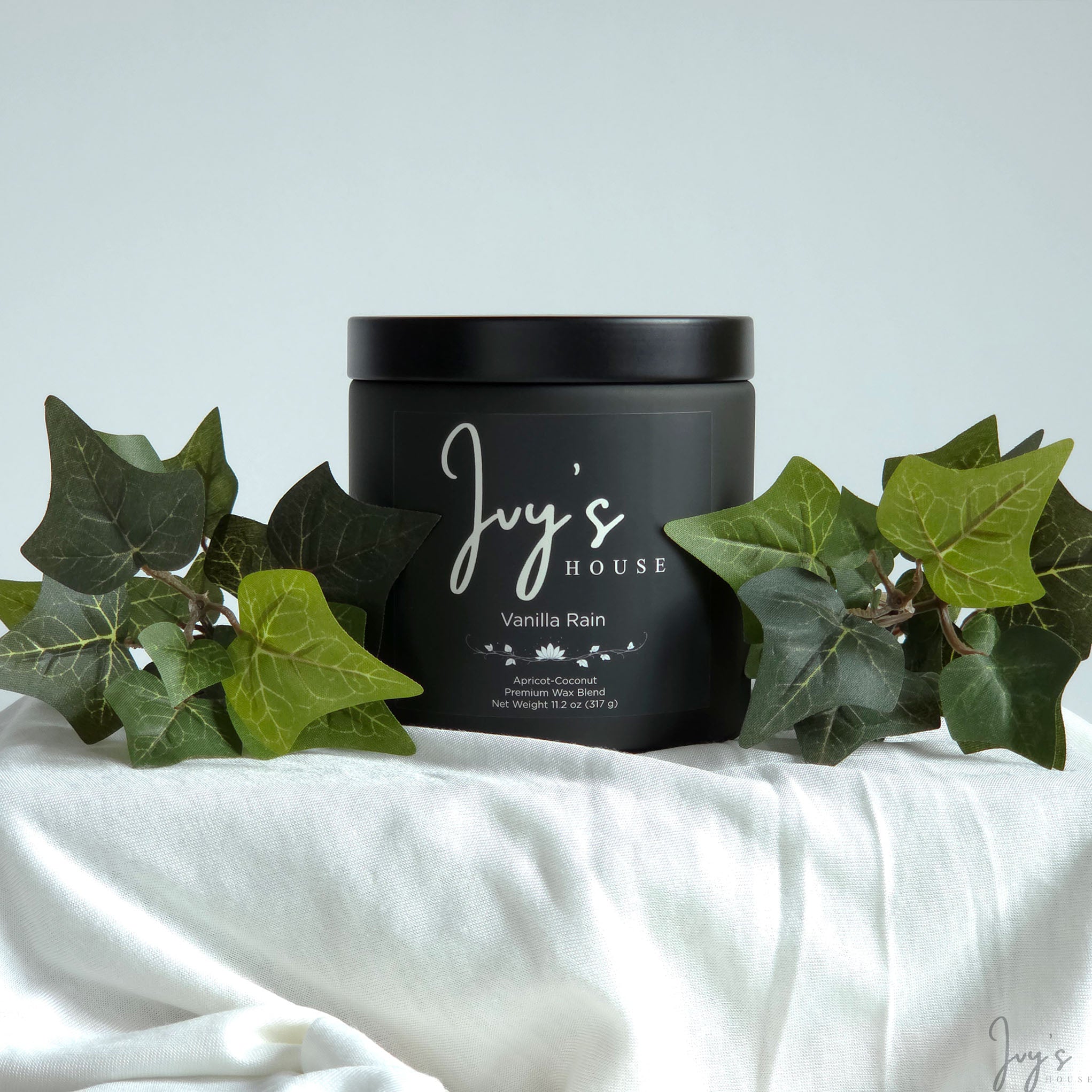 Vanilla Rain premium scented candle by Ivy’s House with ivy leaves on soft white fabric