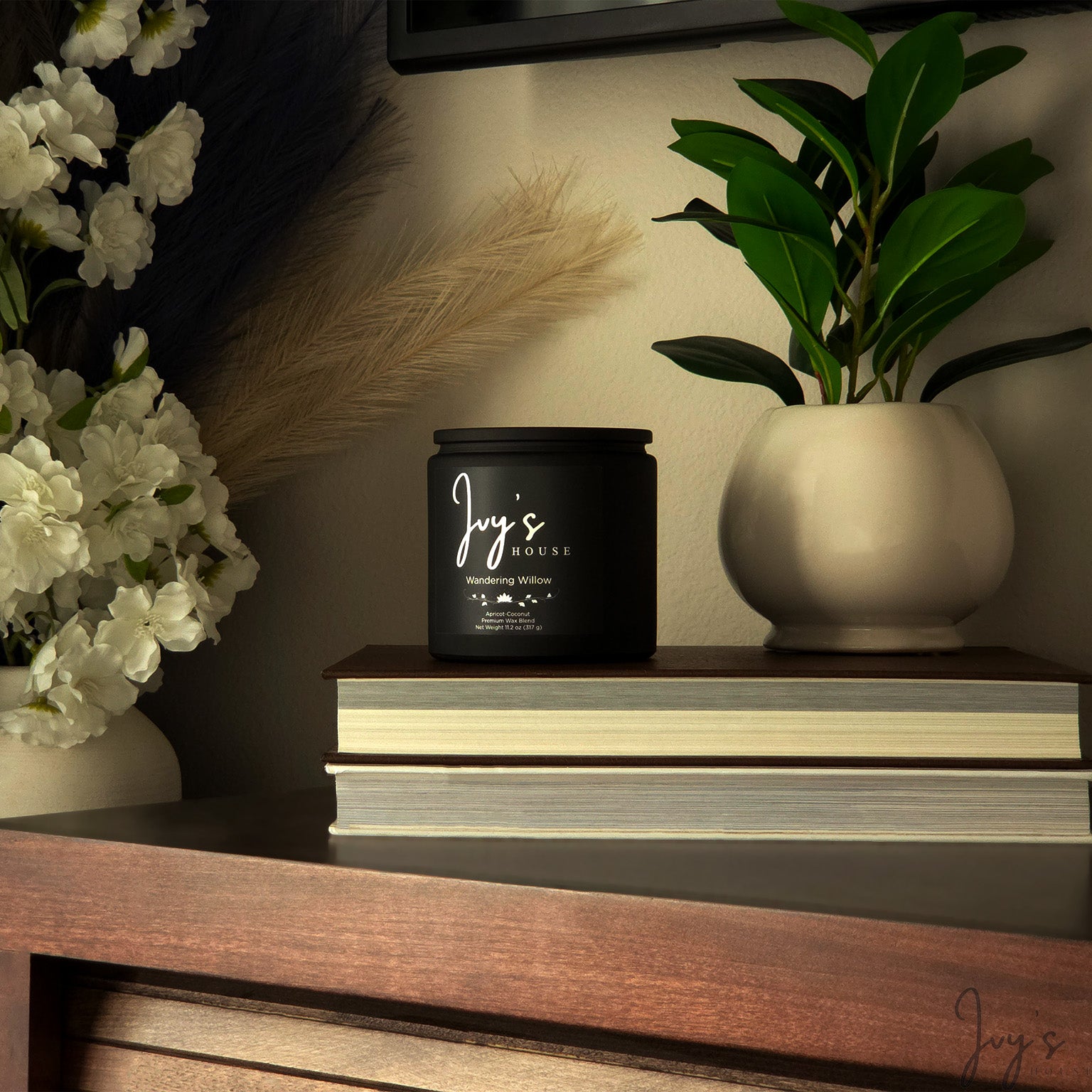 Warm, styled home scene with Ivy’s House Wandering Willow candle, books, and floral decor
